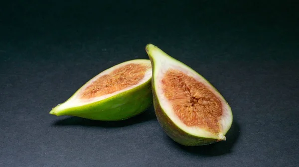 Green figs, one fruit cut into two halves on a light dark background