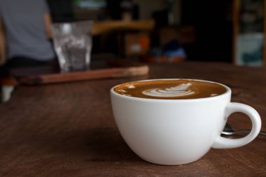 Tahta masadaki bir fincan sıcak latte sanat kahvesi.