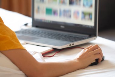 Laptop ve cep telefonuyla çalışan yumuşak odaklı Asyalı bir kadın yatağa uzanıyor, herhangi bir yerde çalışıyor ya da ev konseptinde çalışıyor..
