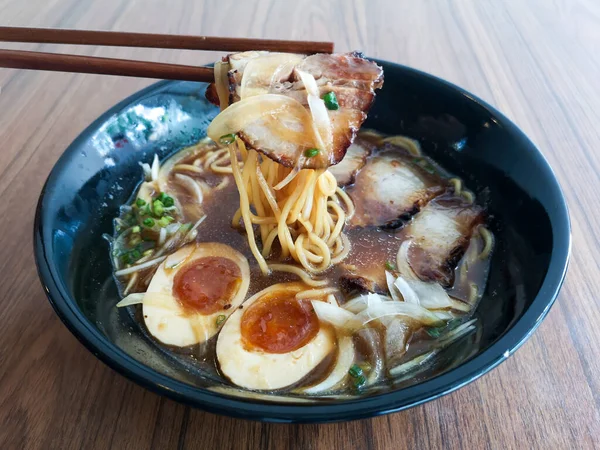 Siyah bir kase Shoyu Ramen eriştesi, ahşap masada domuz eti ve yumurta..