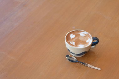 Bir fincan sıcak sütlü kahveyi ahşap masaya koy..