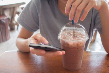 Bir kadın buzlu çikolatalı milkshake içiyor, yaz içecekleri kafenin ahşap arka planında.