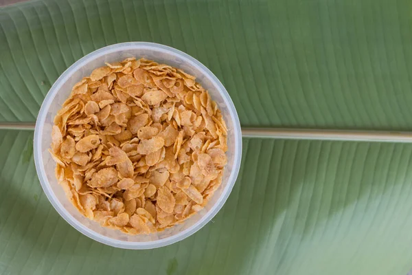 Corn flakes on plastic bowl with green banana leaf background.