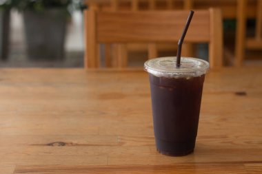 Americano kahvesi, kahve dükkanındaki ahşap masanın üzerinde paket plastik bardakta..