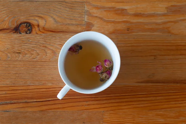 tea made from tea rose petals in a white cup on wooden rustic background.