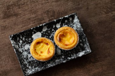 Alüminyum folyo bardakta yumurtalı turtalar ahşap masada, geleneksel Portekiz tatlıları kahve dükkanında servis edilir..