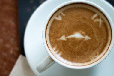 Kahve dükkanının arka planında, ahşap masanın üzerinde bir fincan Latte Art sıcak kahvesi..