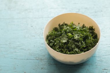 Pastel ahşap masa zemininde beyaz plastik bolluk içinde doğranmış taze kişniş yaprakları..