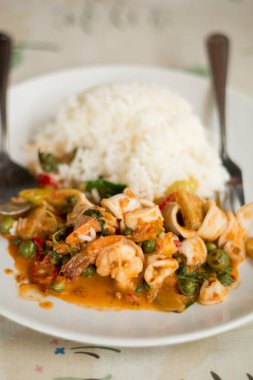 Kızarmış fesleğen yaprakları ve beyaz tabakta karışık deniz ürünleri..