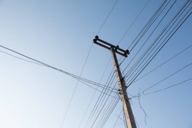 Mavi gökyüzü arka planında elektrik kabloları olan elektrik direği.