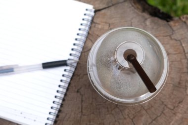 Ahşap çalışma masasında defter ve kalemle buzlu kahve içtikten sonra, sıkı çalışma konsepti..