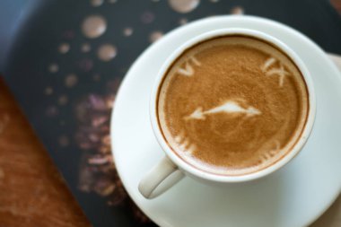 Kahve dükkanının arka planında, ahşap masanın üzerinde bir fincan Latte Art sıcak kahvesi..