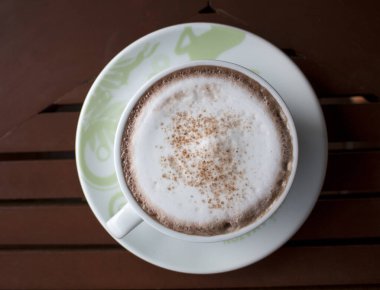 Kahve dükkanının arka planında, ahşap masanın üzerinde bir fincan Latte Art sıcak kahvesi..