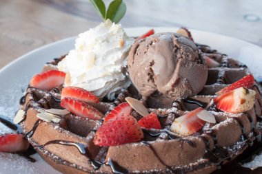 Çikolatalı dondurmayı waffle ve ahşap masa arkasında taze çilek ile kapat..