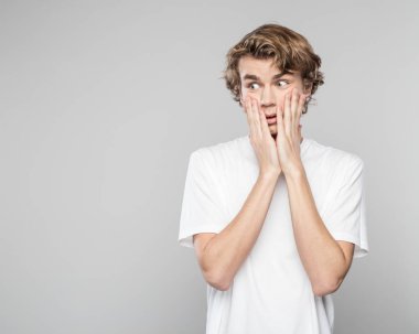 Elleri ile gri arka plan beyaz t-shirt ayakta yanaklarda giyen genç adam korkuttu.