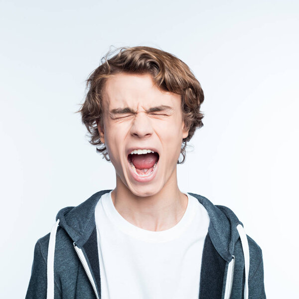 Teenage boy wearing t-shirt and hoodie screaming with eyes closed. Studio shot against white background. 