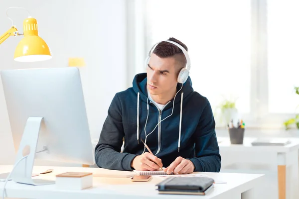 Müzik ve Not almak için dinleme hoodie evde, Masa başında oturan genç adam. Öğrenci veya serbest kavramı.