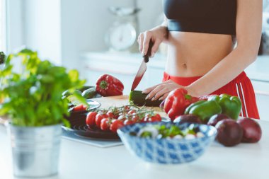 Evde mutfakta ayakta ve sebze salatası yapmak spor kıyafetleri giyen genç kadın. Elleri, tanınmayan kişi yakın çekim. 
