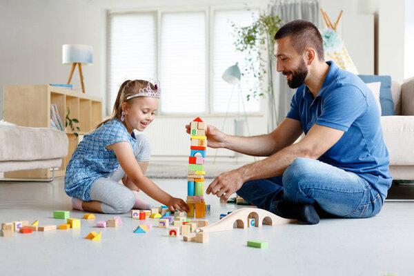 Отец с дочерью играют с блоками вместе дома, сидя на полу в гостиной
. 