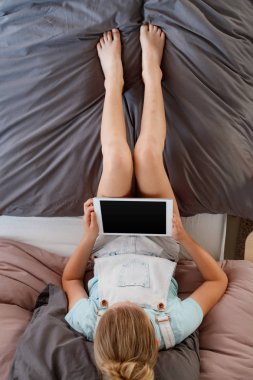 Yatağında oturmuş ve dijital tablet kullanma kızın üstten görünüm. 