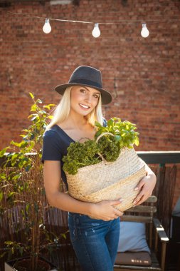 Kale, fesleğen ve yeşil sebze sepeti tutan güzel genç kadın açık bir kadeh. Kameraya gülümseyen. Yavaş hayat kavramı. 