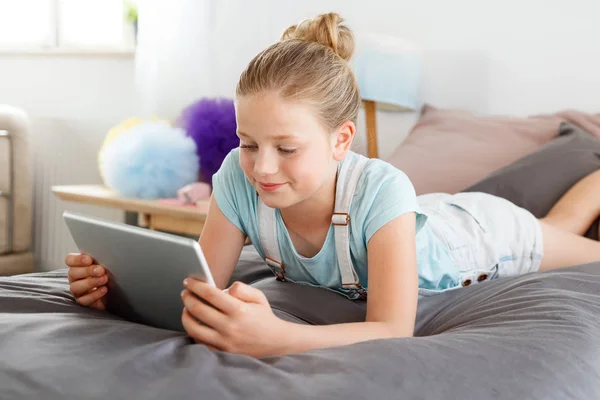 Kız yatak odasında yüzüstü yatarken ve dijital tablet kullanma.