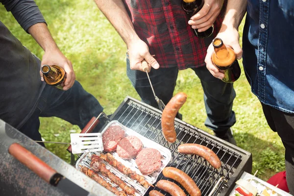 Açık atış Barbekü partisi zevk, sosis ve hamburger ızgara üç arkadaş. Yüksek açılı görünüş, tanınmayan insanlar. 
