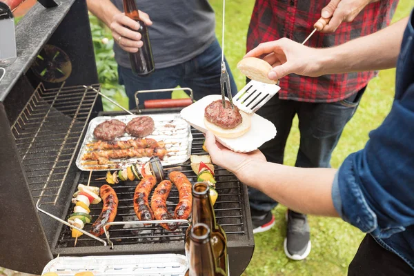 Açık atış Barbekü partisi zevk, sosis ve hamburger ızgara üç arkadaş. Yüksek açılı görünüş, tanınmayan insanlar. 