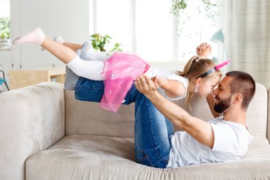 Baba kızını evde piggybacking, oturma odasında kanepede yatan, eğleniyor.