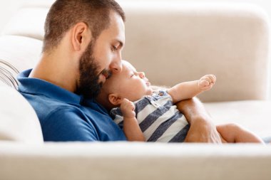 Mutlu genç baba kanepe karınca evde oturan ve onun erkek bebek kucaklayan. 