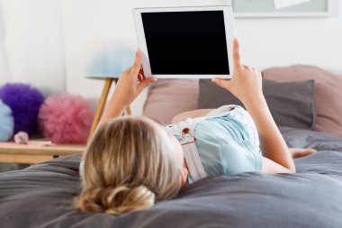 Arkadan görünüm kız yatak odasında yatarken ve dijital tablet kullanma. 