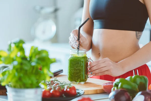 Yeşil smoothie tutan spor kıyafet giyen kadın. Ellerin ve bally kapatın. Tanınmayan kişi.