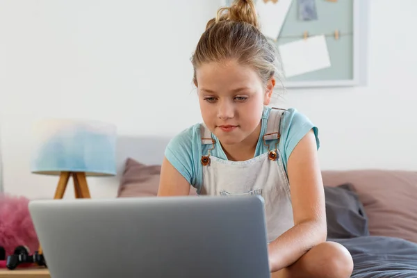 Girl learning on bed in her room and using a laptop.