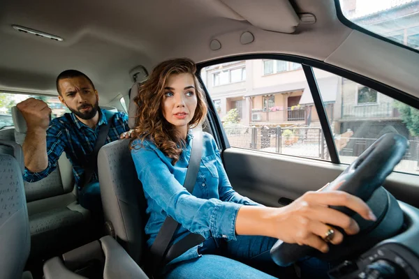 Angry passenger arguing with female uber driver, screaming and gesturing with fist.