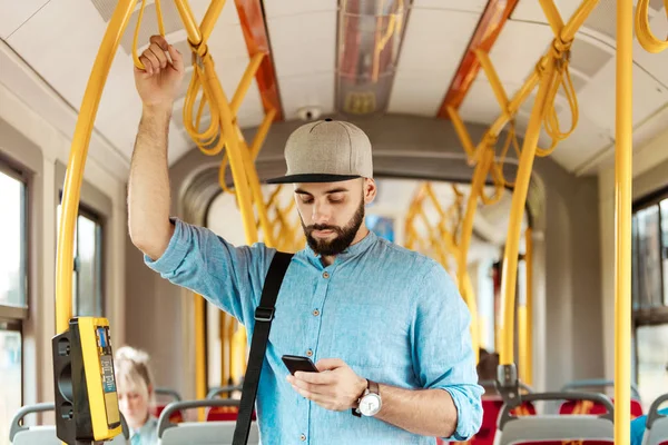 Genç adam manifatura otobüsteki akıllı telefon üzerinde sakallı.
