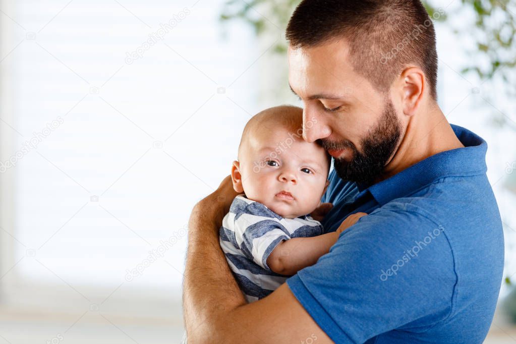 Happy young father holding his baby boy at home. 
