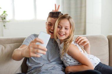 Mutlu ve salon ve akıllı telefon kullanarak alma selfie kanepede oturan kız. 