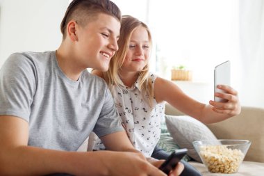 Mutlu ve salon ve akıllı telefon kullanarak alma selfie kanepede oturan kız. 