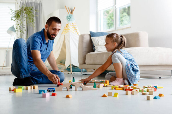 Отец с дочерью играют с блоками вместе дома, сидя на полу в гостиной
. 