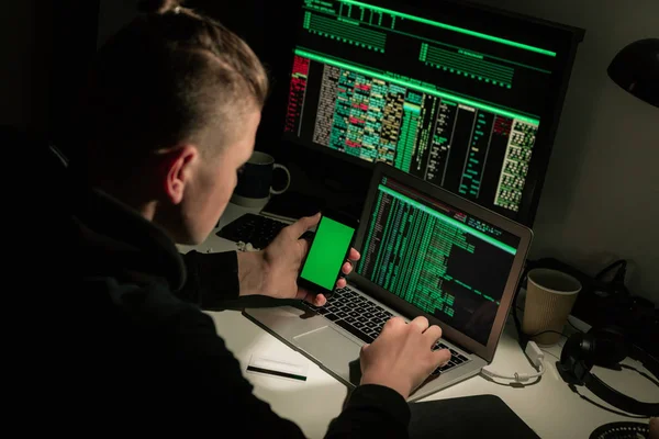 Hombre Joven Sentado Escritorio Oscuridad Utilizando Ordenador Portátil Teléfono Inteligente —  Fotos de Stock