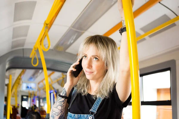 Smiling young woman talking on mobile phone in city bus.