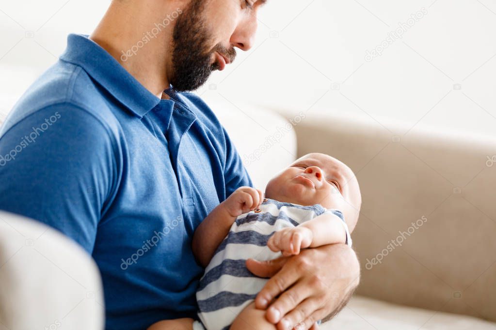 Young father holding his baby boy, sitting on sofa, children crying.