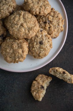 Koyu arka plan. Pembe bir sınır ile beyaz bir plaka üzerinde çikolata ile gevrek lezzetli ev yapımı yulaf ezmeli kurabiye. Tanımlama bilgisi yarım.