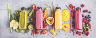 Düz-lay şişelerde taze tropikal meyve ve beton zemin üzerine superfoods ile renkli smoothies