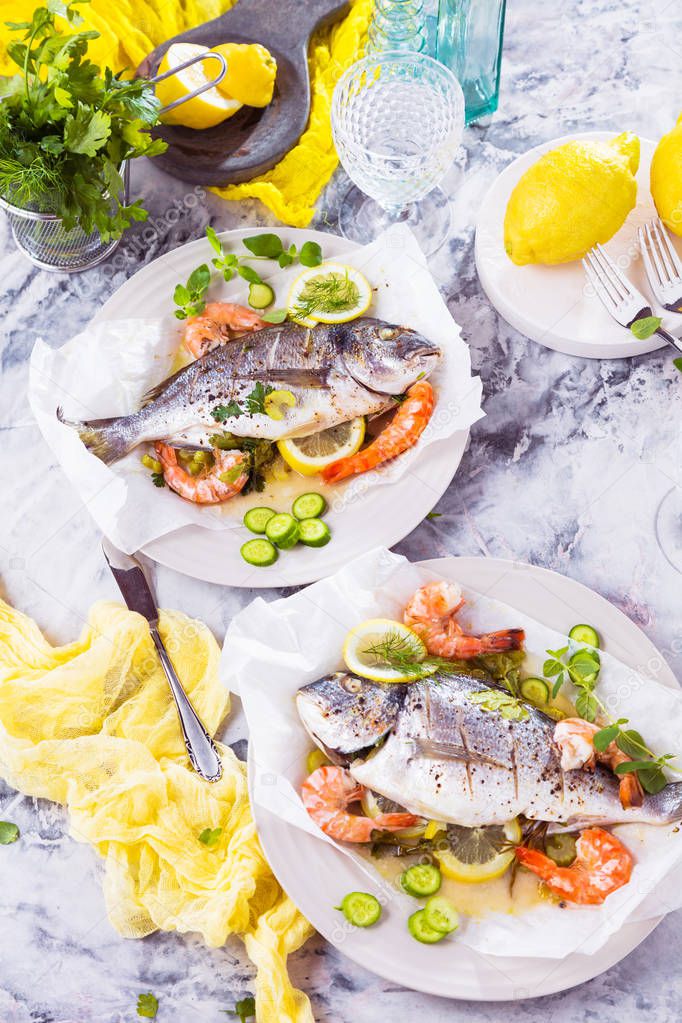 delicious sea bream fish with lemon and fresh Prawns, fresh parsley and spinach on white platter on 