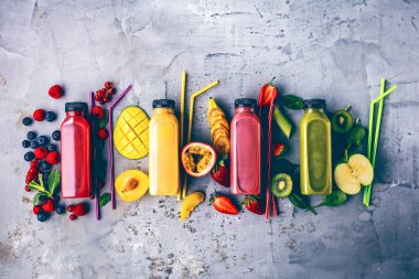 Düz-lay şişelerde taze tropikal meyve ve beton zemin üzerine superfoods ile renkli smoothies