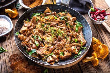 Kırsal siyah ahşap bir masada, dökme demir bir tavada kızarmış mantarlar.