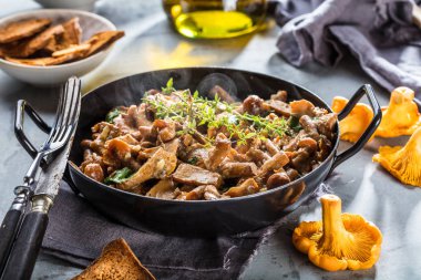 Kırsal siyah ahşap bir masada, dökme demir bir tavada kızarmış mantarlar.