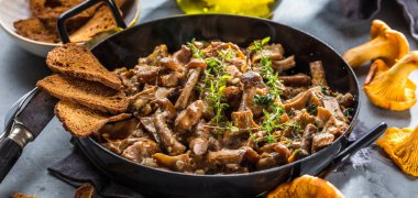 Kırsal siyah ahşap bir masada, dökme demir bir tavada kızarmış mantarlar.