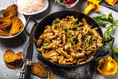 Kırsal siyah ahşap bir masada, dökme demir bir tavada kızarmış mantarlar.